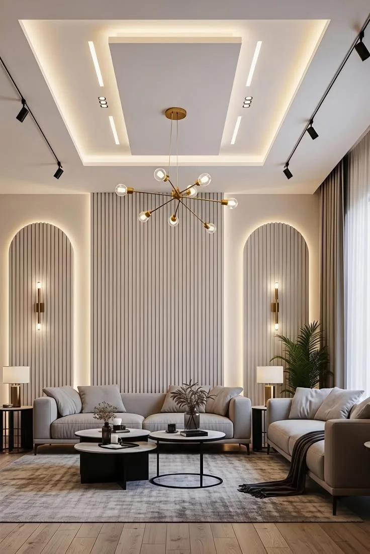 A living room with a stepped false ceiling, cove light, linear lights, a chandelier and backlit fluted wall panels