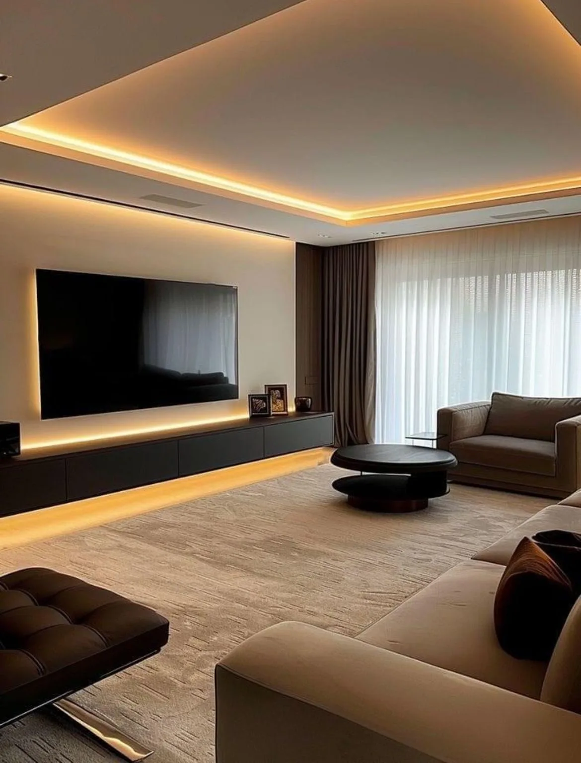 A finished living room with warm cove backlighting, a wall-mounted TV, floor-length curtains and a ceiling AC grille