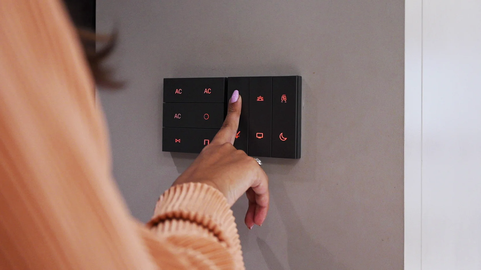 A hand pressing a scene button on a black AHA keypad mounted on a plain wall